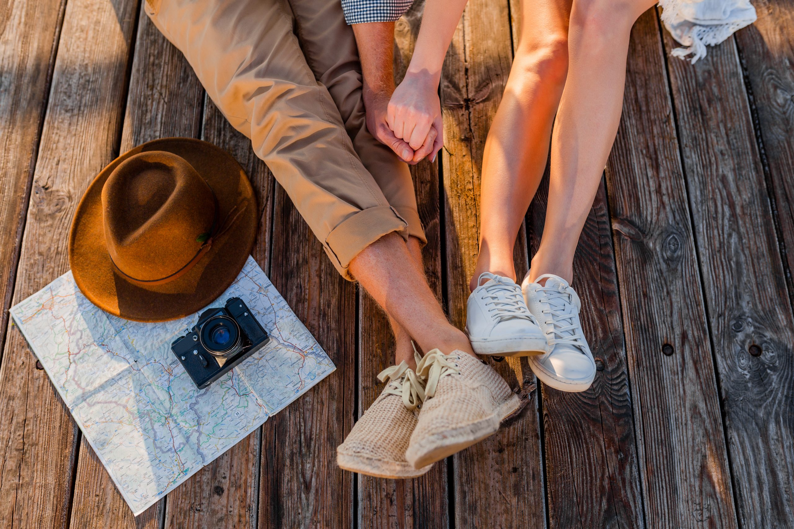 view from above legs of couple traveling in summer dressed in sneakers, man and woman boho hipster style fashion having fun together, map, hat, photo camera, sightseeing, footwear fashion